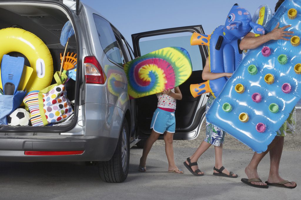 Father and two children (6-11) unloading beach accessories from car