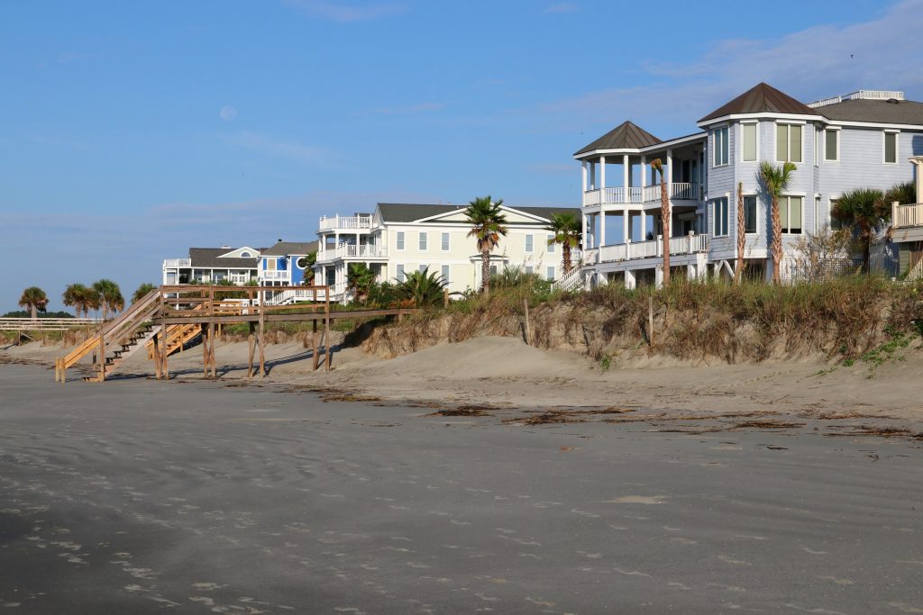 Marine landscape with oceanfront neighborhood in Charleston, South Carolina during low tide. Morning view with palm trees between houses for vacation rentals and footprints on a wet sand.