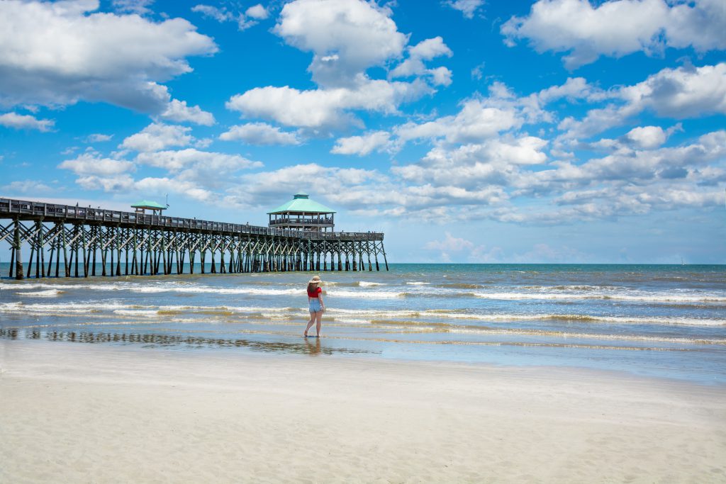 Girl walking on the beautiful beach. Woman relaxing on summer vacation by the ocean. Cloudy sky and pier in the background. Folly Beach, South Carolina USA.